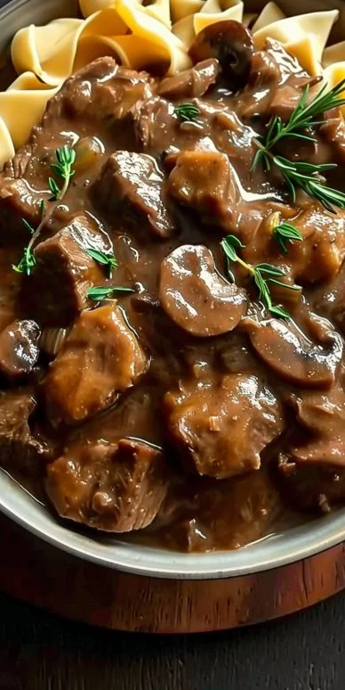 Bowl of beef stew with mushroom gravy, garnished with fresh herbs.